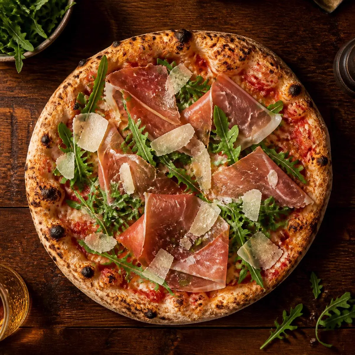 Pizza con prosciutto crudo, rucola e scaglie di grana vista dall'alto su un tavolo di legno